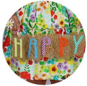Image: flowered skirt background with woman's hands holding a string of letters spelling happy.