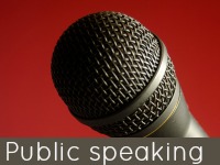 Image: A black microphone on red background. Text: Public Speaking