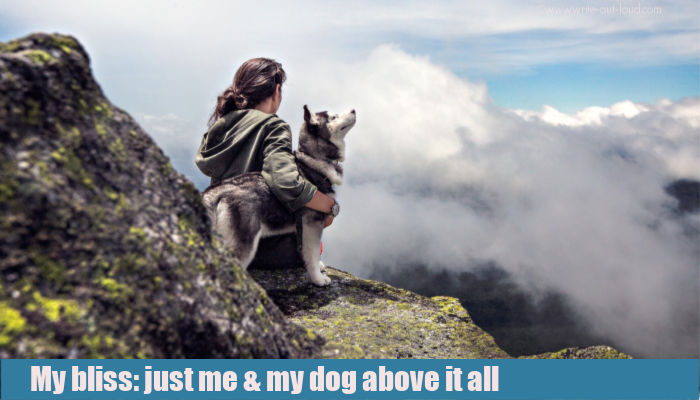 Young woman with her dog sitting on a mountain ledge high above the clouds.
